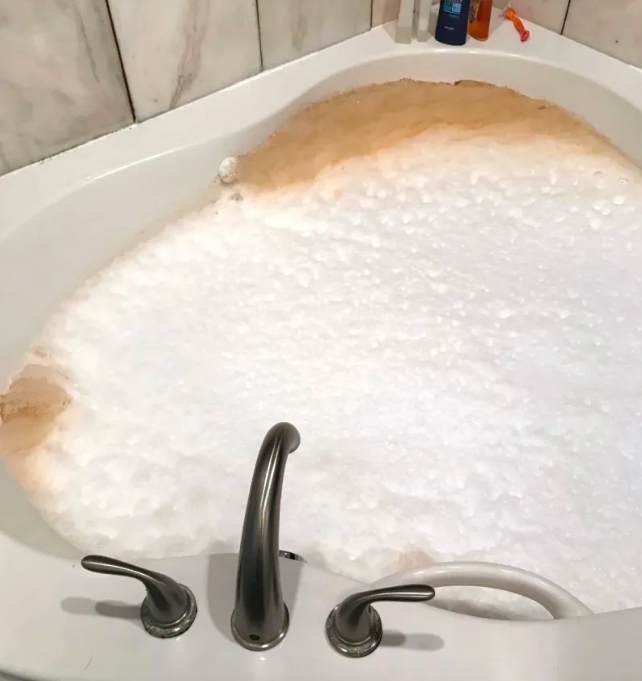 Bath filled with bubble cleaner, with brown bubbles on sides from dirty jets 