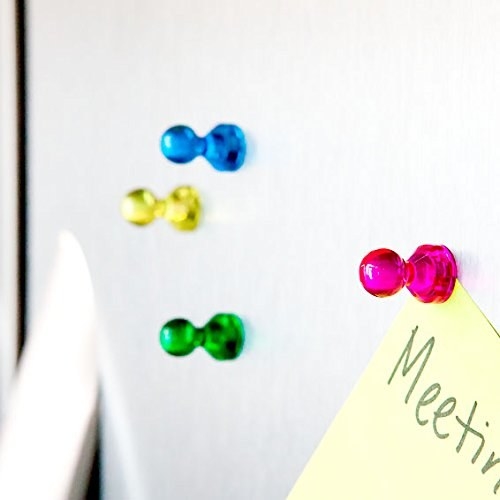 Colorful magnetic pushpins on a whiteboard with a corner of a note visible