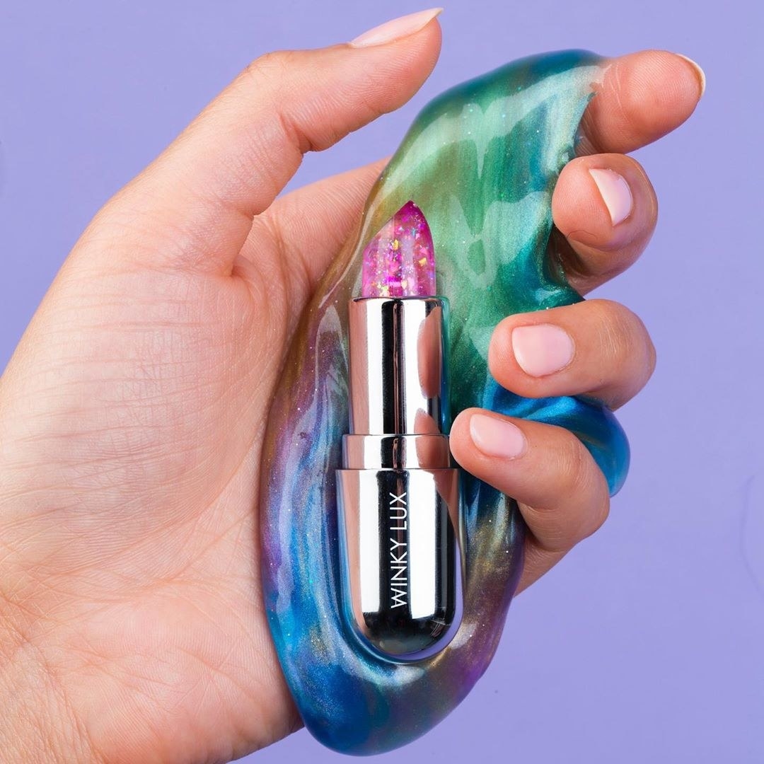 Hand holding the transparent pink lip balm, which has a chrome case