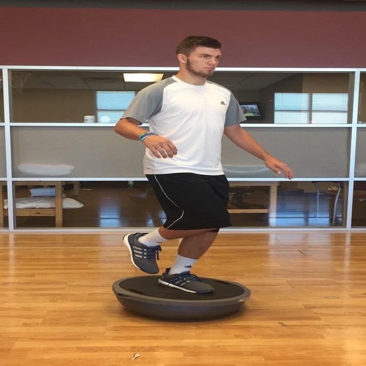 Reviewer standing on the trainer on one foot with the balance ball-like top on the group
