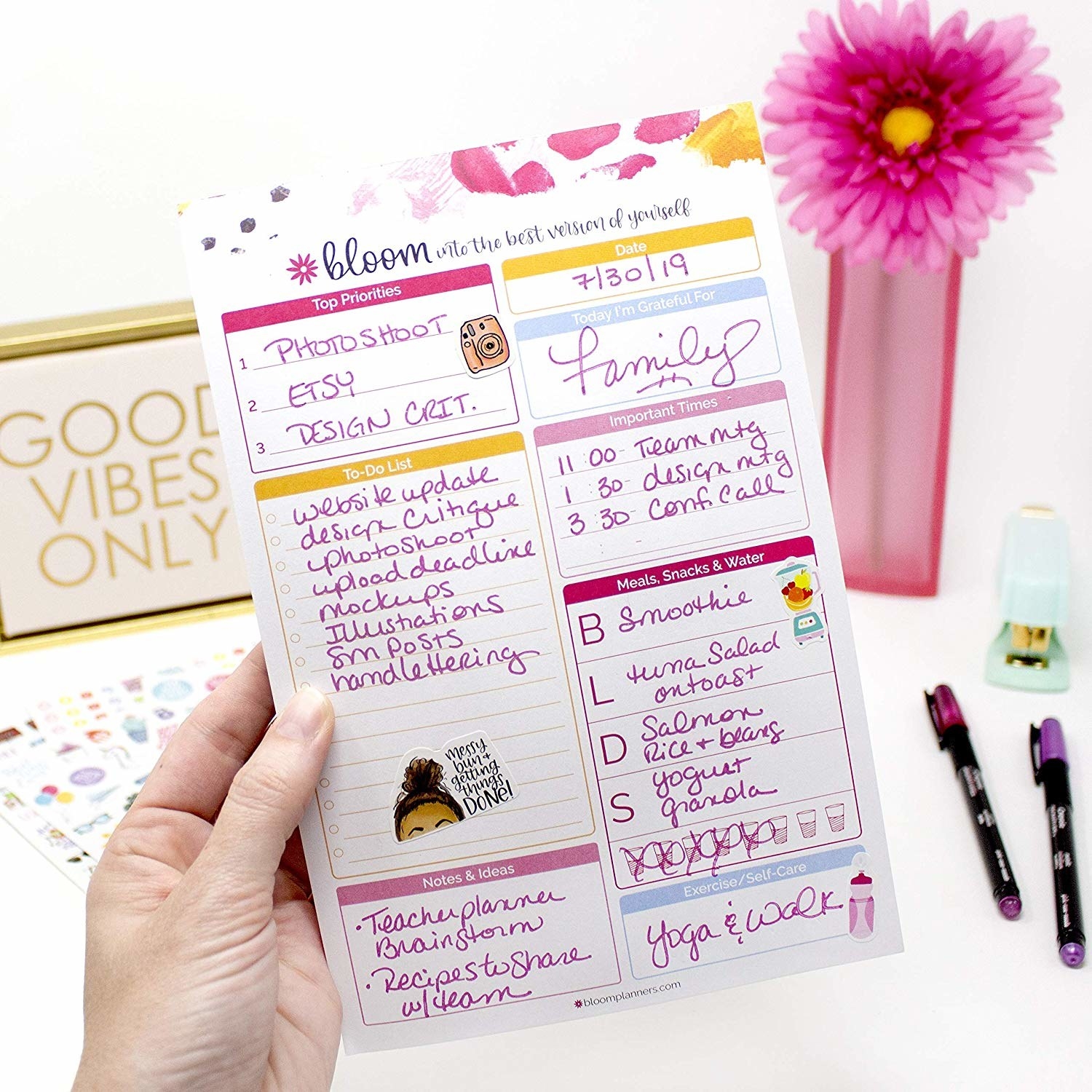 A hand holding up a sheet of the planning pad in the pink and yellow color scheme