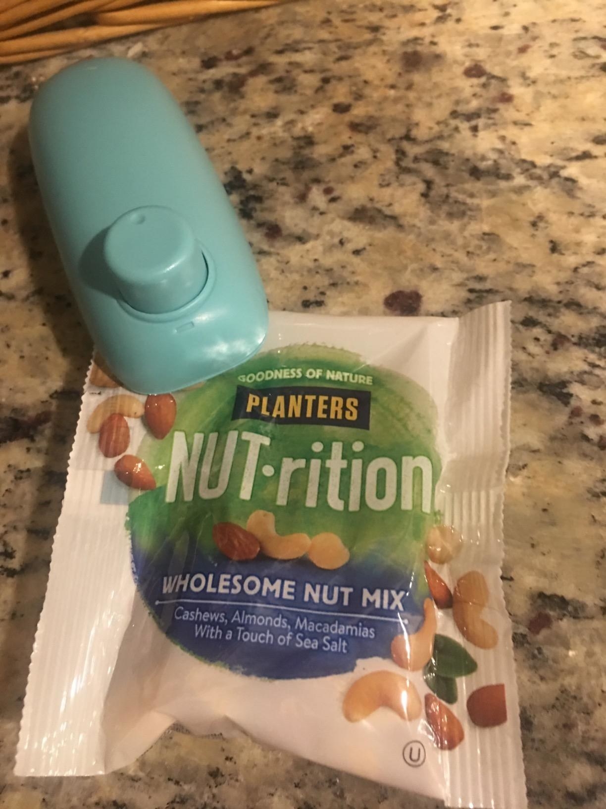 A reviewer using the handheld sealer, which has a single button on top, to re-seal a bag of mixed nuts