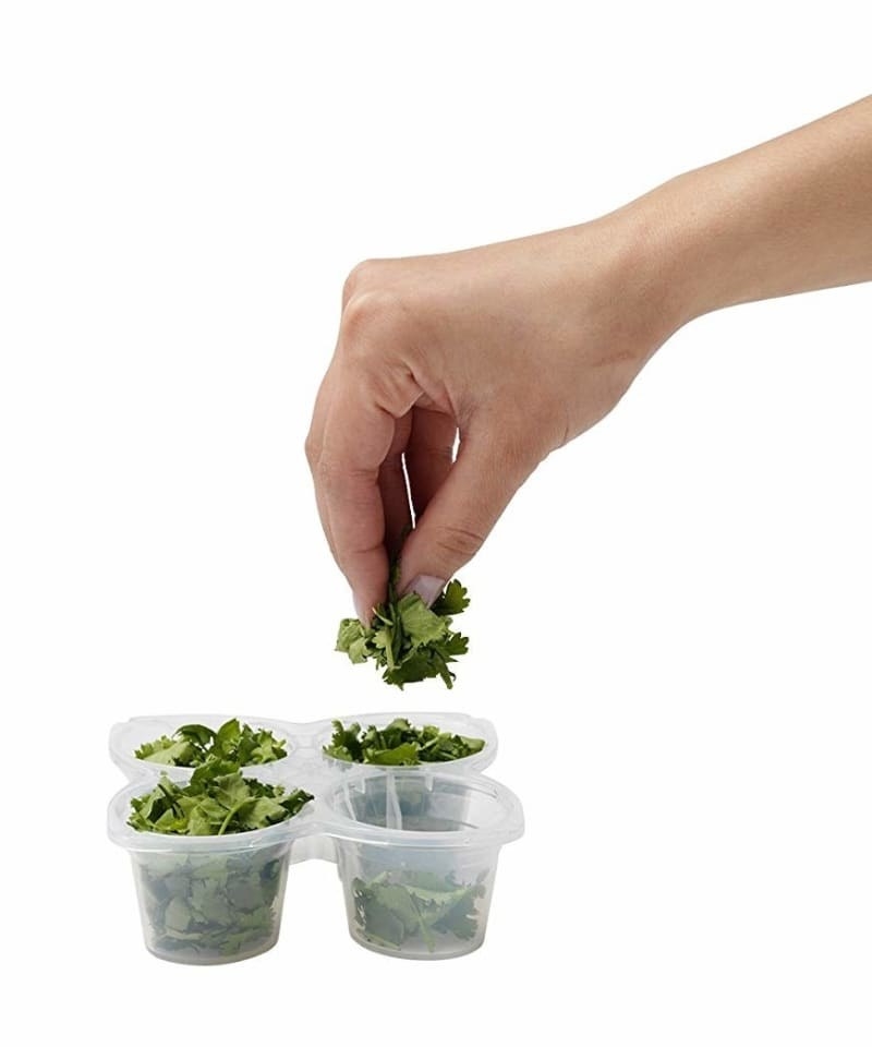 A tray with four connected cups filled with herbs and a model's hands taking a few herbs out of one of the cups