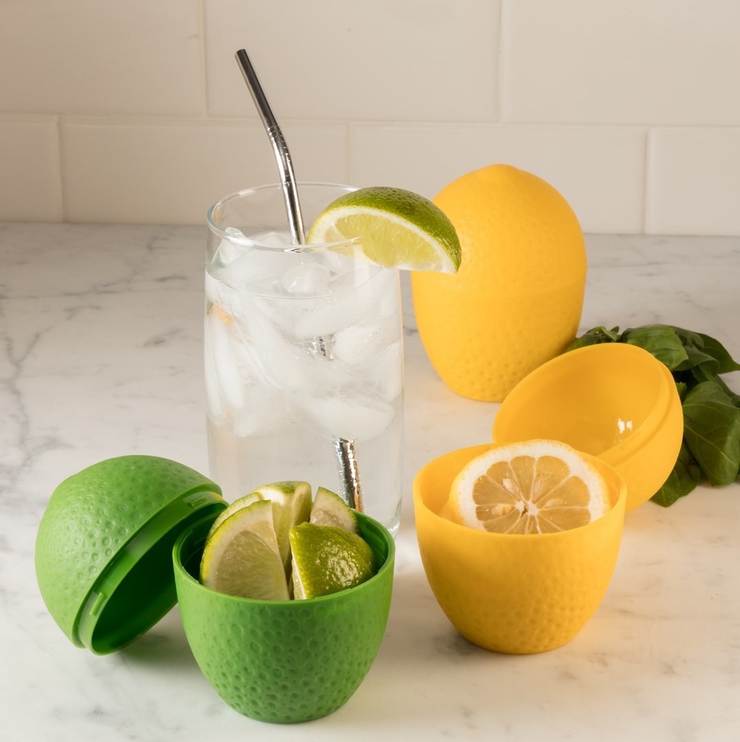A lemon-shaped container holding a sliced lemon and a lime-shaped container holding a sliced lime