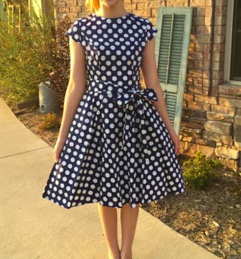A reviewer wearing the knee-length dress in blue and white polka dots