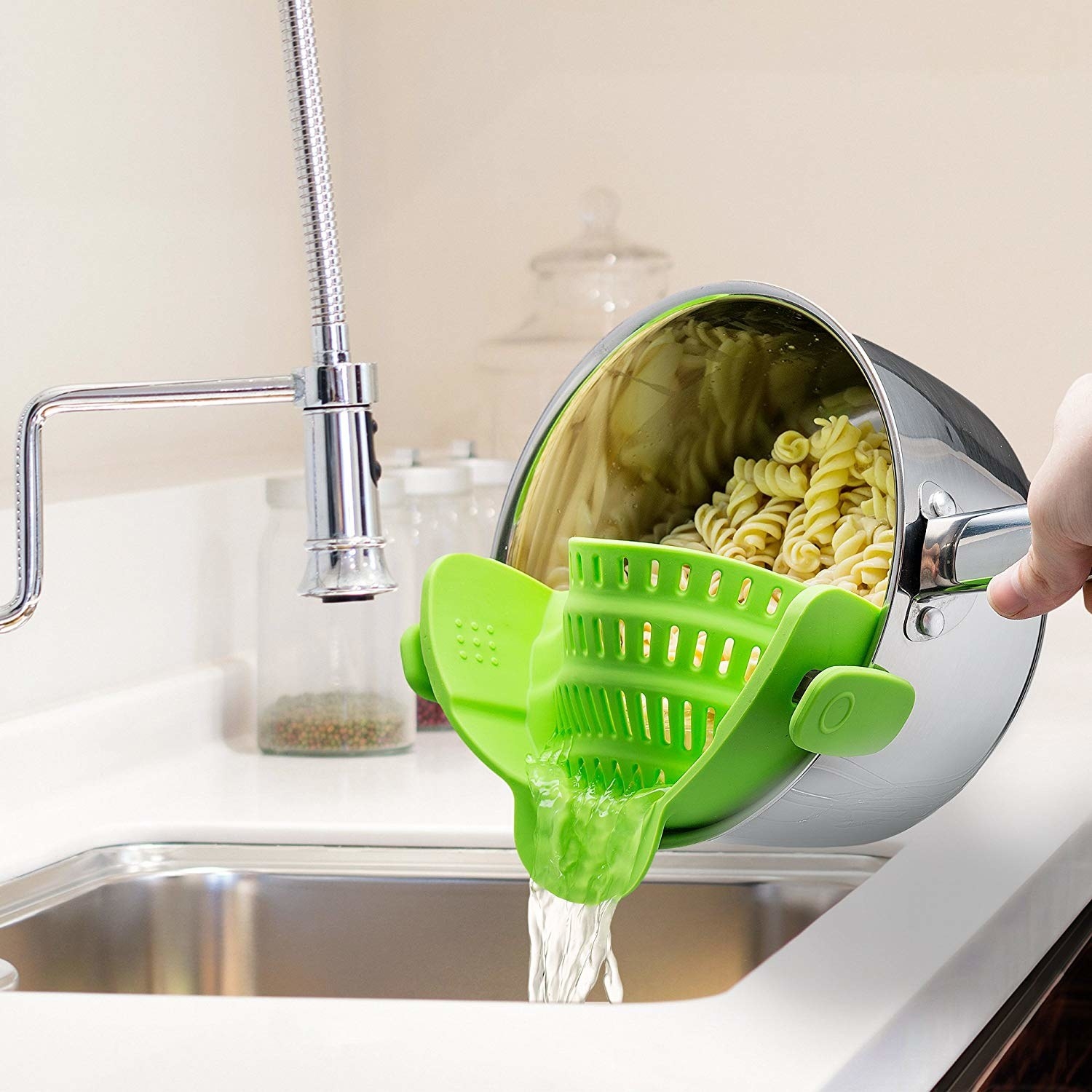 Product photo showing green clip on strainer straining pasta into a sink 