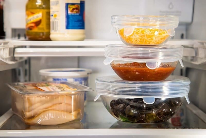 Three silicone lids on a small, medium, and large bowls filled with food in a fridge