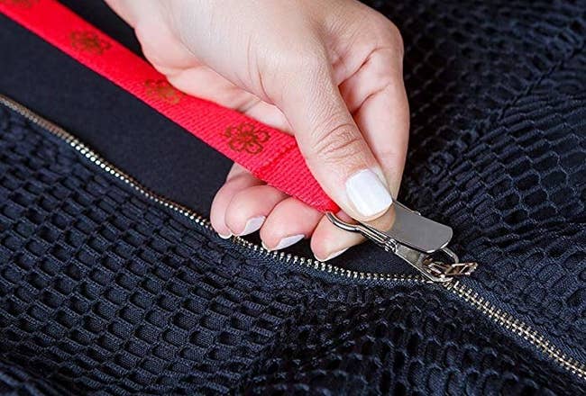 A hand pulling the Zippuller's long strap attached to a zipper