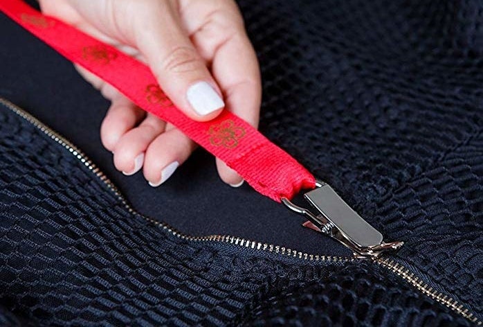 A hand pulling the Zippuller's long strap attached to a zipper