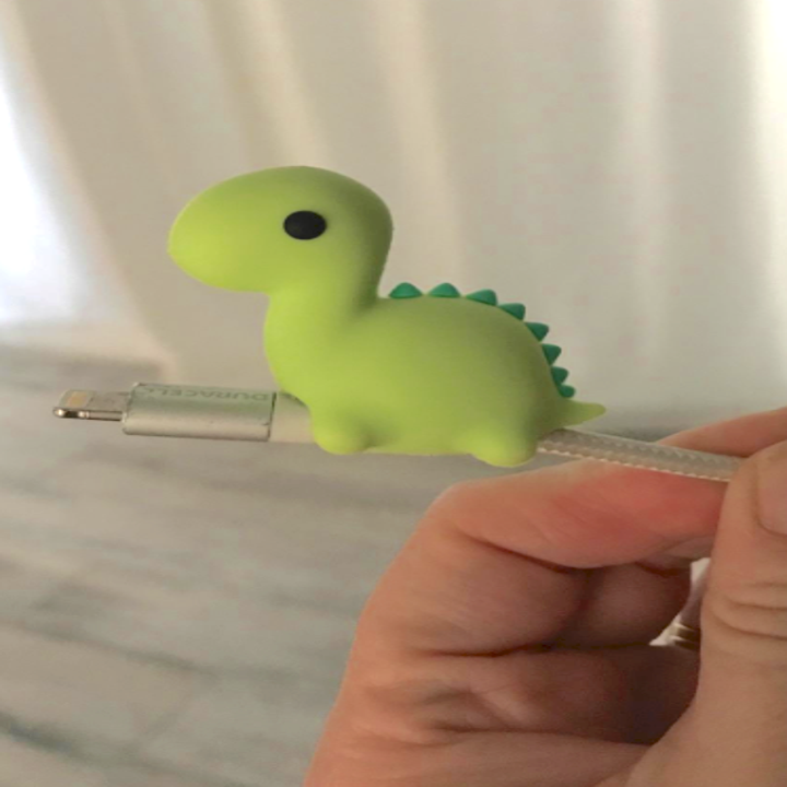 close-up of a green dinosaur-shaped cable bite on a phone and/or laptop charger