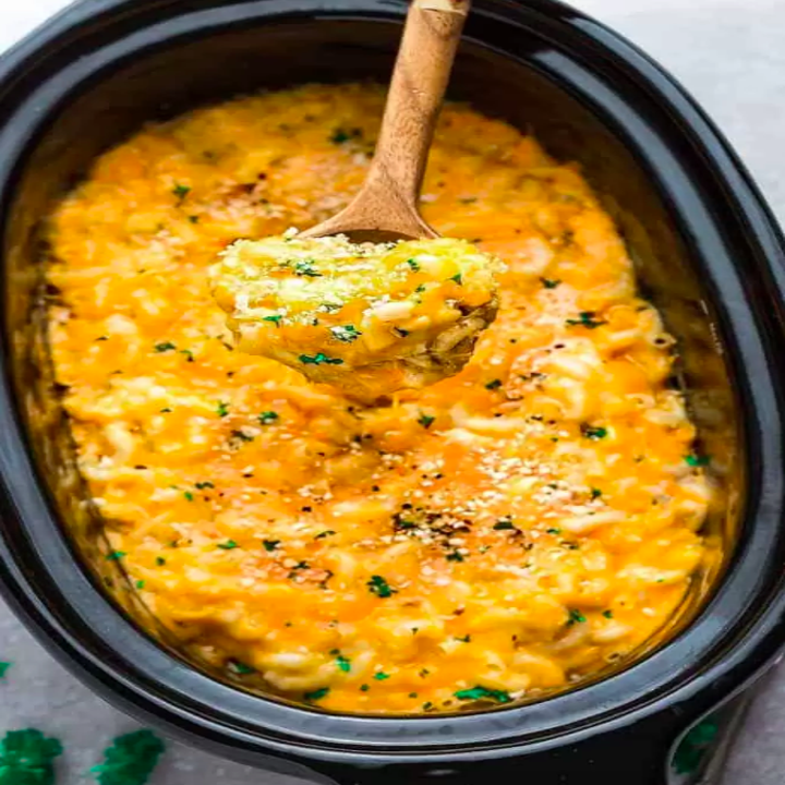 Cheesy, baked macaroni and cheese in a crockpot, with a wooden spoon lifting a serving