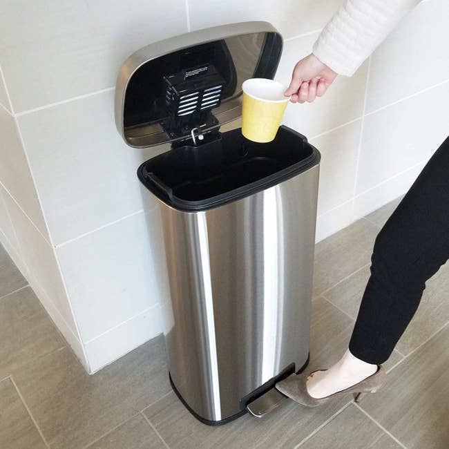 A model stepping on the trashcan opener and throwing out a disposable cup