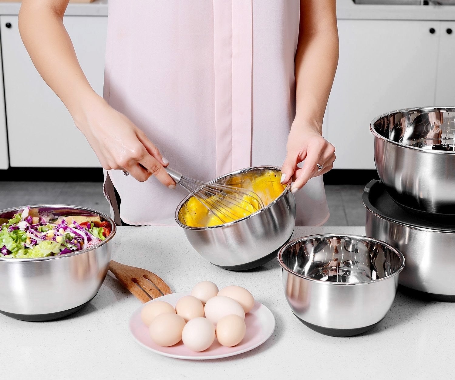 A model whisking eggs in one of the bowls, with other ingredients in the others