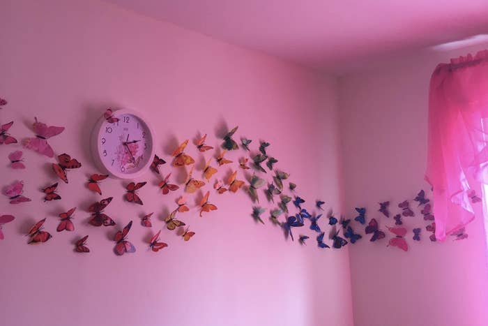 A pink wall with a line of 3D butterflies that look like they&#x27;re flying by the wall.