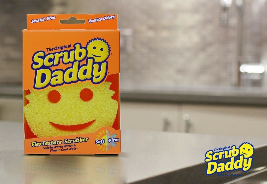 The Scrub Daddy sponge in a box. It&#x27;s a yellow sponge with cutouts that create a smiling face.
