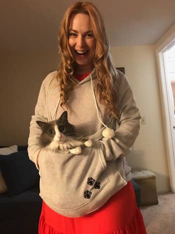 Reviewer wearing the gray hoodie with a gray and white cat lying in the pouch