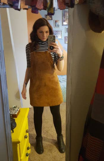 reviewer wearing the pinafore with a striped turtleneck and black tights