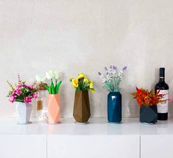 A set of five different geometric vases filled with flowers and sitting on the top of a white desk