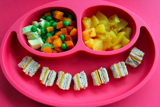 A reviewer showing the three divided sections of the placemat. Two are small and round for chopped sides and one is a long section in the middle for sandwiches and larger foods.