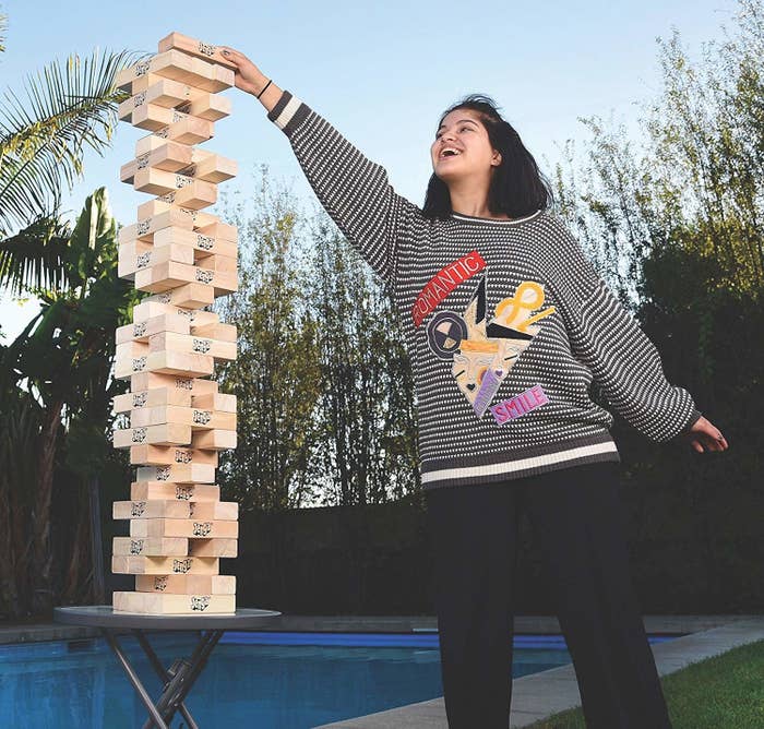 A person playing Jenga that has been put on a small table. With the help of the table, game towers over their head