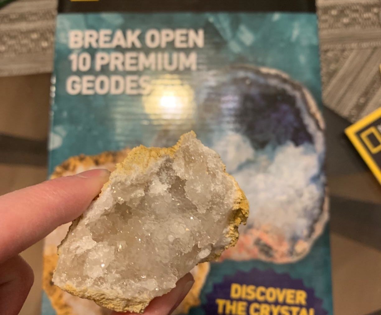 hand holds up open geode in front of box