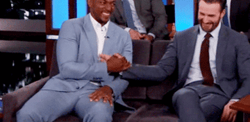 Anthony Mackie and Chris Evans dapping but ending with their pointer fingers out, thumbs up, and other fingers linked