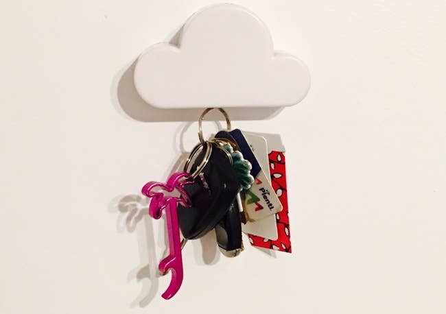 A minimalist cloud magnet tacked to a wall holding car keys 