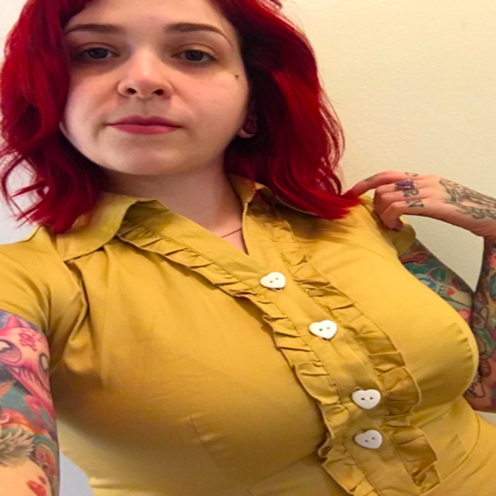 A reviewer wearing the dress in mustard yellow, close up on the white heart buttons on a ruffled placket