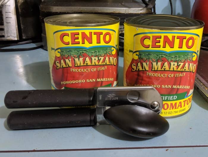 Two cans of Cento San Marzano tomatoes and a can opener sit on a kitchen counter