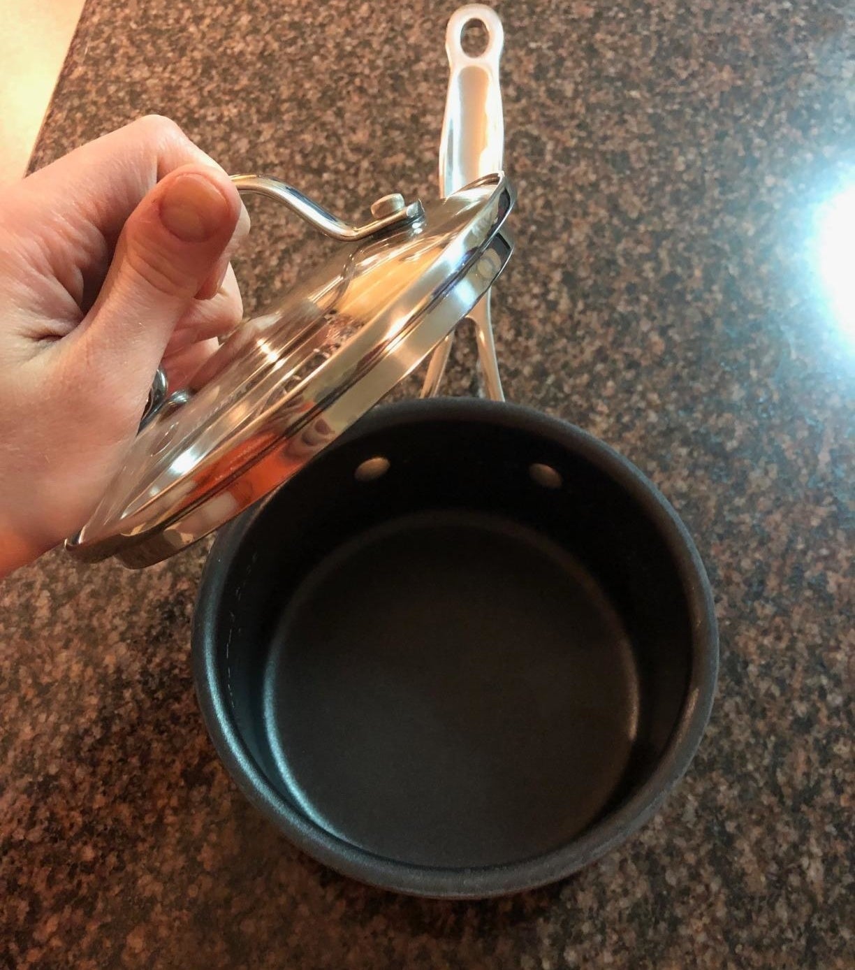 Hand lifting lid of a small saucepan on granite countertop