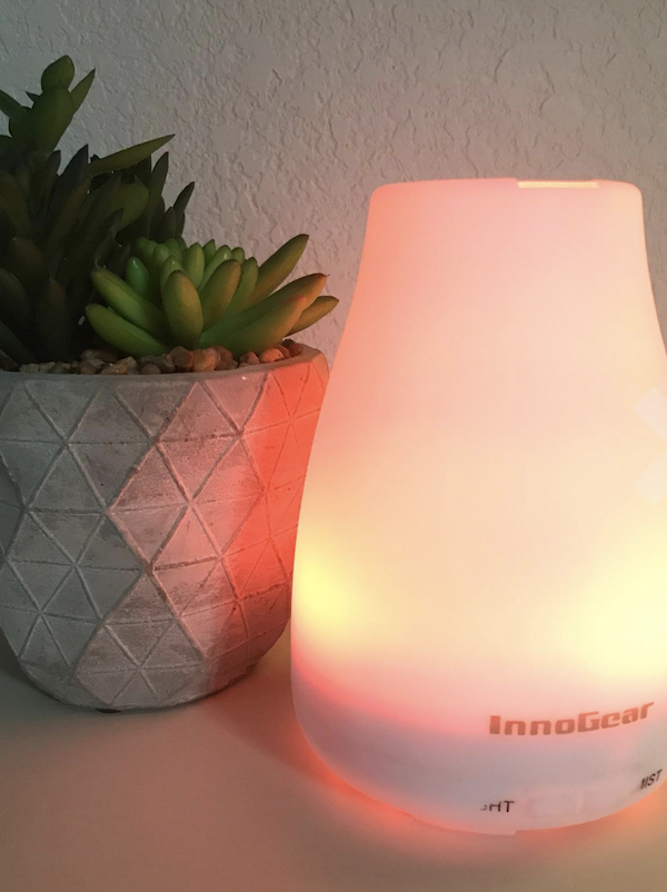 A plastic white humidifier is lit with an orange light. It&#x27;s sitting next to a green succulent in a grey ceramic pot.