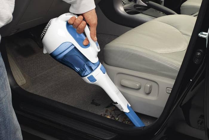 person vacuuming the floor of their car with the cordless vacuum