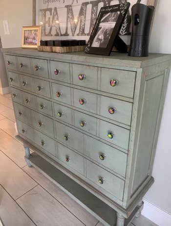 reviewer photo of a pale green wooden dresser with the colorful crystal knobs on the drawers