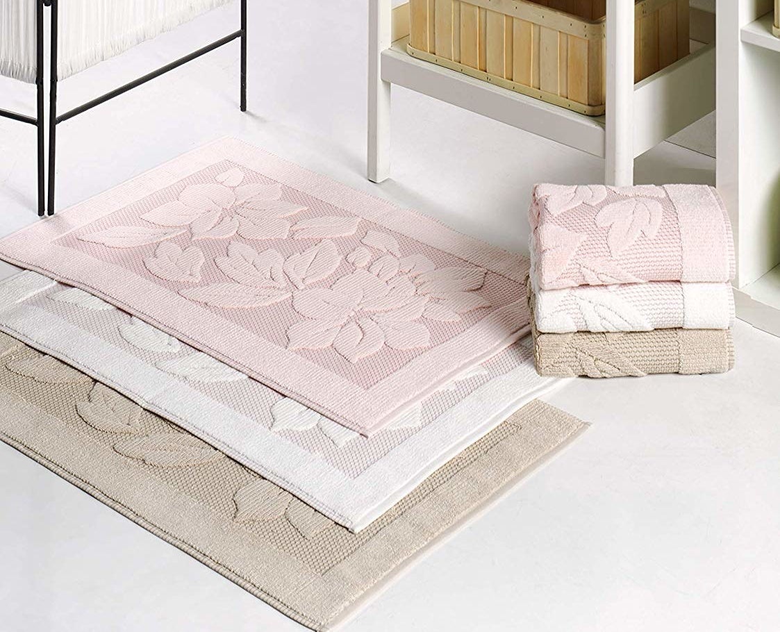 lifestyle image of three stacked bath mats in pink, white, and tan