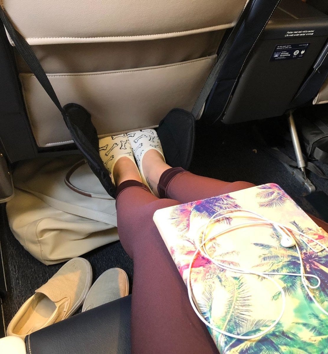 reviewer photo of the black foot hammock on a plane with feet in them