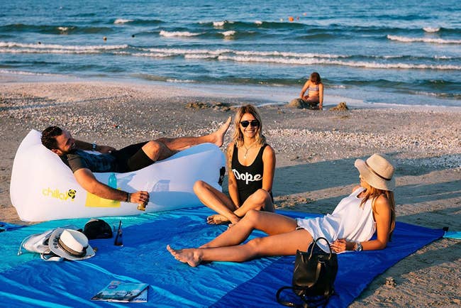models sitting on a multi-colored blue blanket on a beach