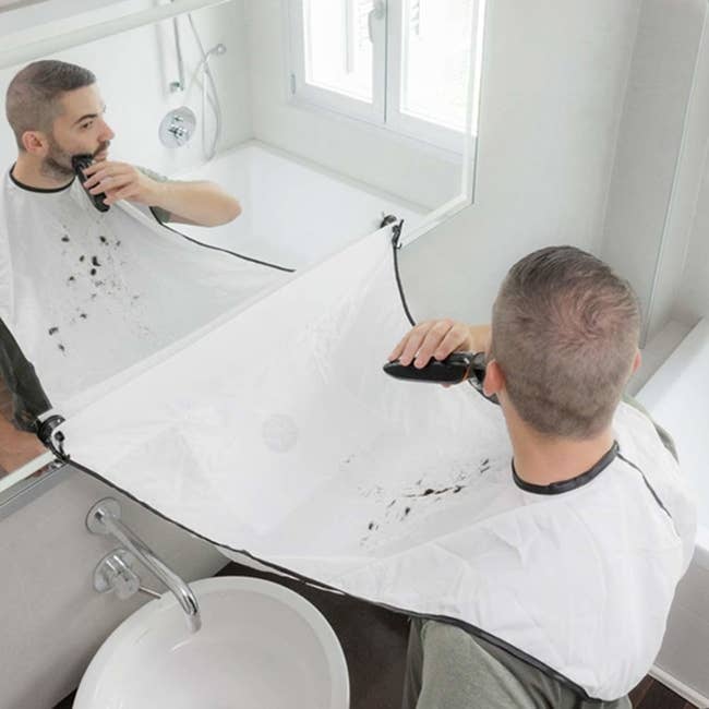 Person shaving with cape around neck and attached to bathroom mirror 