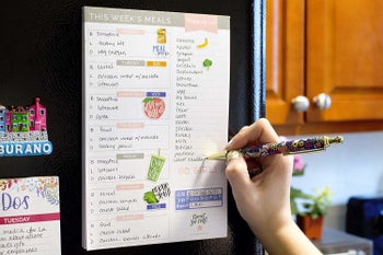 a hand writing on the pad, which is mounted on the fridge with magnets