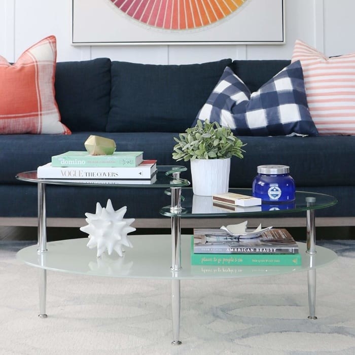 Oval-shaped glass coffee table with frosted bottom shelf and two smaller shelves overlapping at the top in a living room. 