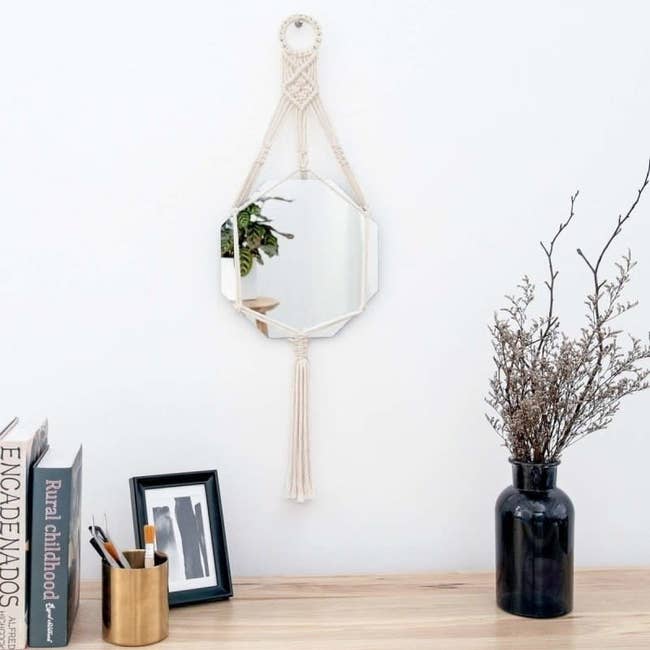 Small hexagon shaped ivory macrame mirror hanging from a wall 
