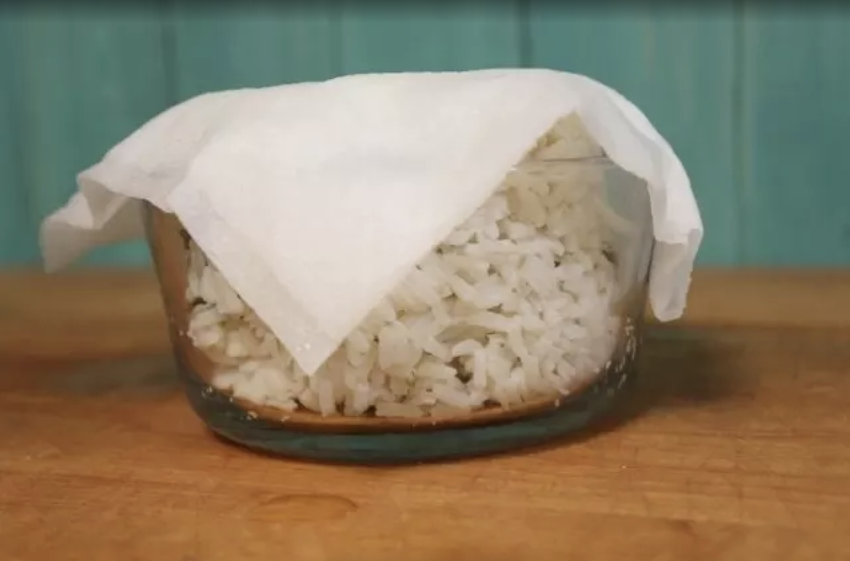 A bowl of white rice reheating in the microwave with a wet paper towel draped over it