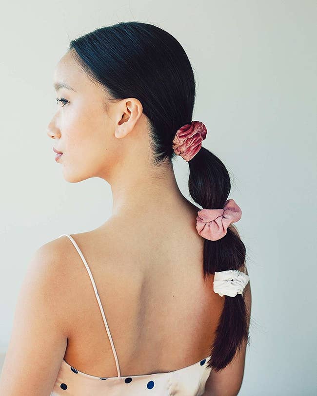 Model with a long ponytail with three scrunchies along the length in dark pink, light pink, and white