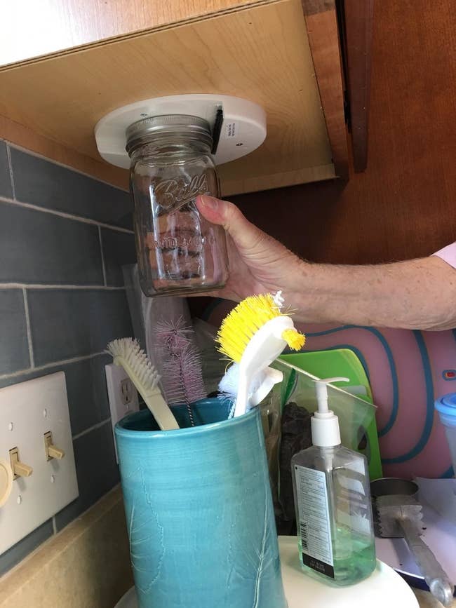 Reviewer using the jar opener, which they've attached to the bottom of a cabinet, to open a mason jar