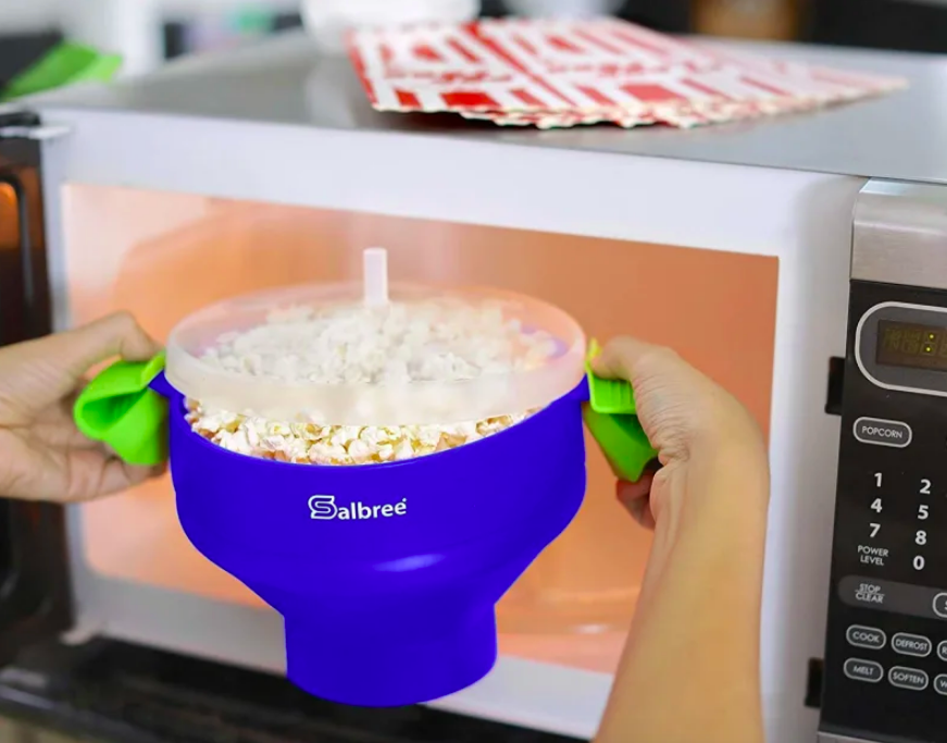 Popped popcorn coming out of the microwave inside covered silicone bowl 
