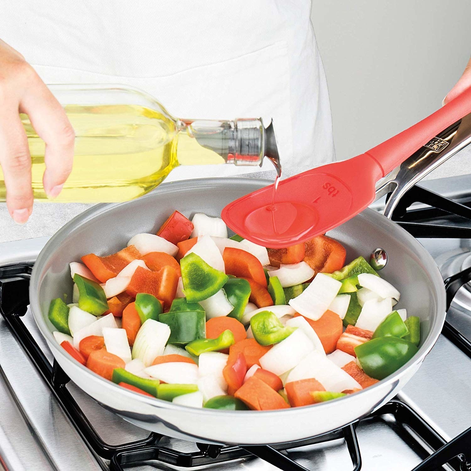 Person sautéing vegetables and pouring oil over the veggies with the measuring spatula 
