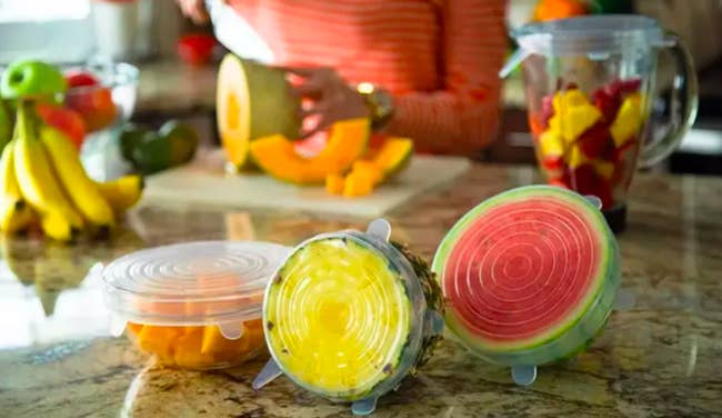 A bowl of of sliced fruit, half a pineapple, and watermelon all covered with the adjustable silicone covers 