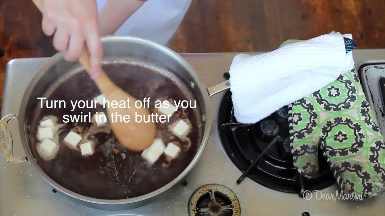 A cook swirling pats of butter into a stovetop steak sauce