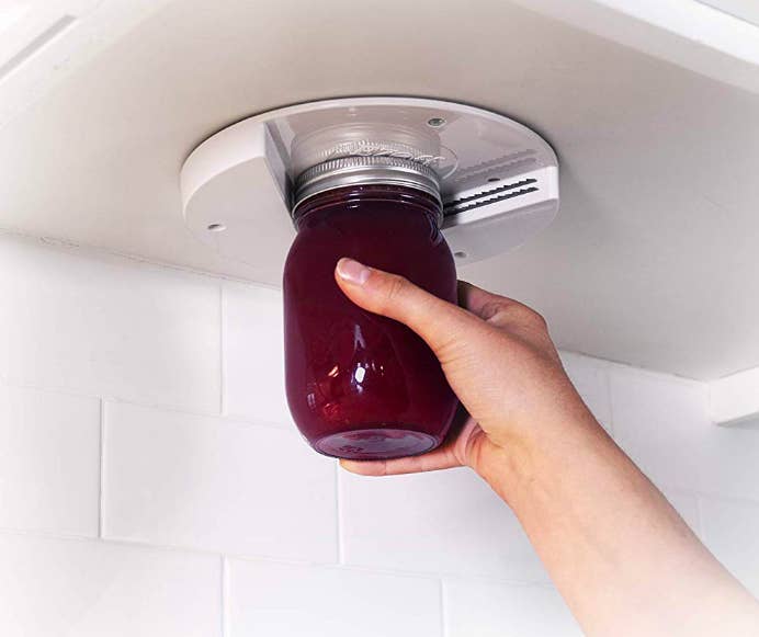 Jar opener attached to bottom of kitchen cabinet being used to open jam container