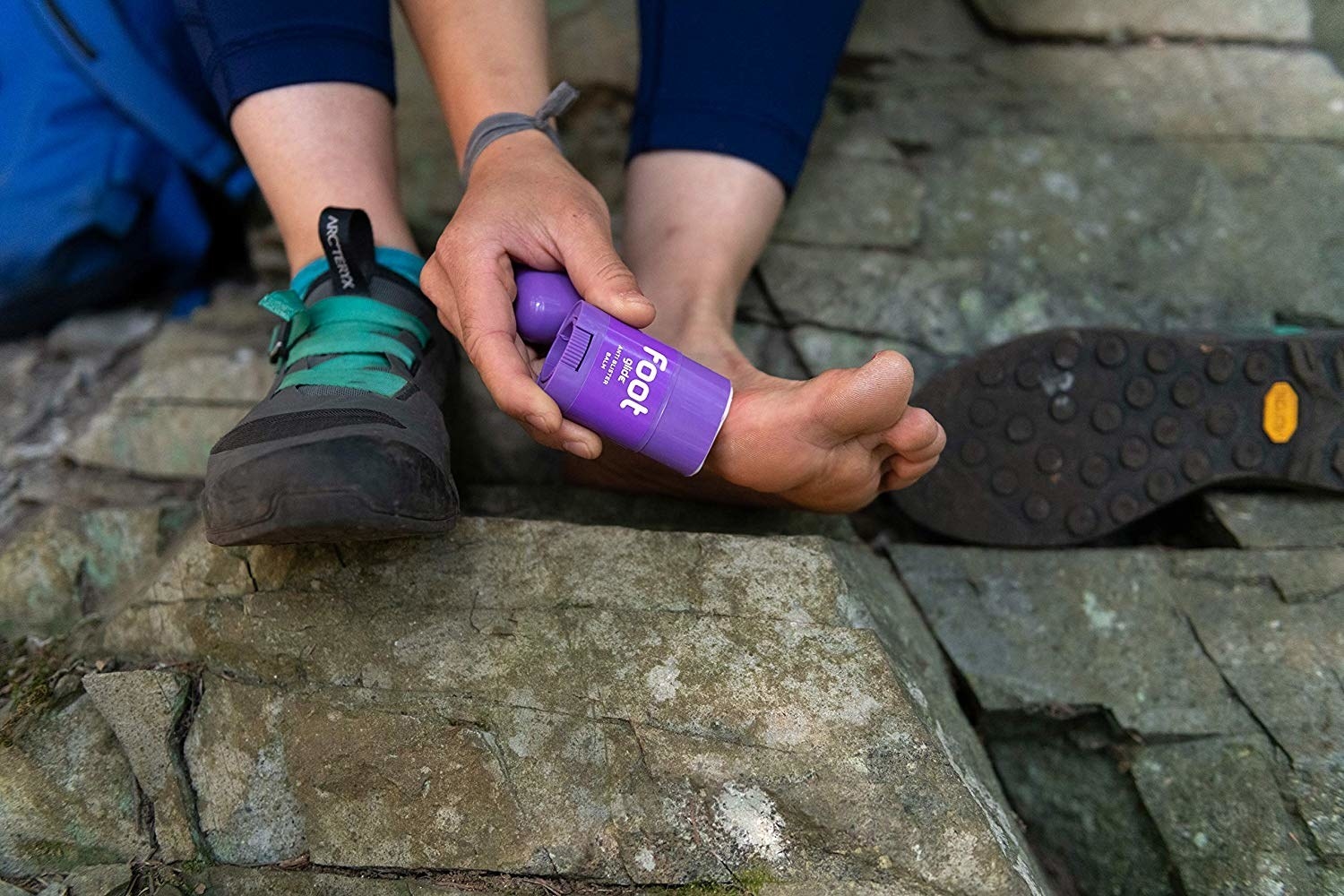 Person applying product to foot while hiking 