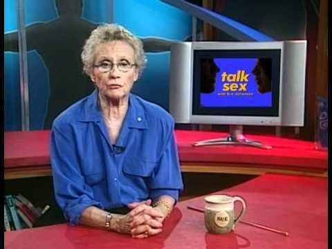 Sue Johanson in a blue shirt, sitting at a red desk on the set of her TV show Talk Sex 